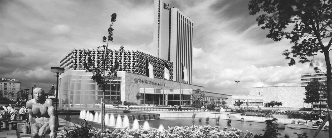 2 deutsche Architekturen Schwarz-weiß-Foto eines Brunnens vor einem Gebäude, das eine ruhige und elegante Atmosphäre vermittelt.