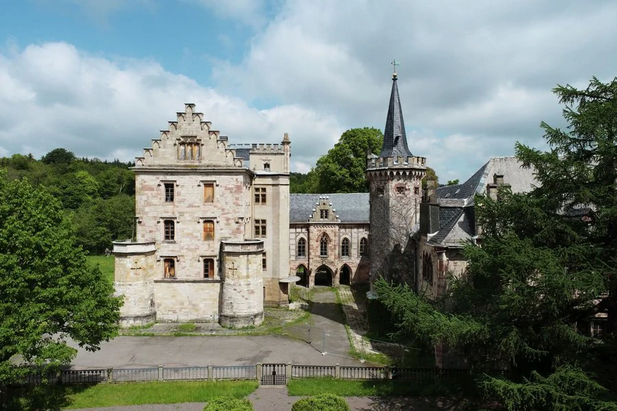 Luftaufnahme eines Schlosses mit einem Turm und einem Innenhof, umgeben von grüner Landschaft.