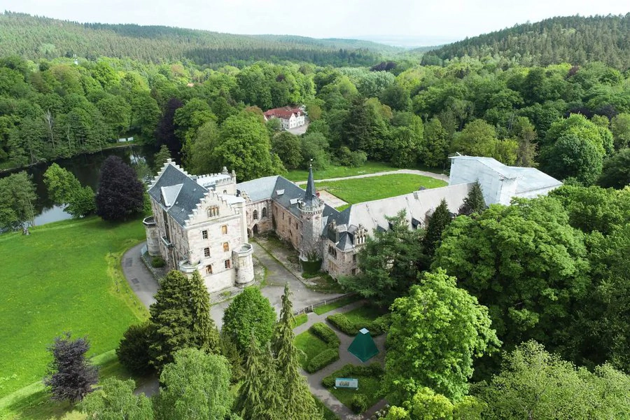 Luftaufnahme eines Schlosses, umgeben von üppigen Bäumen, die eine malerische Landschaft bilden.