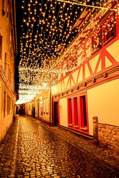 Julia Fischer, Postgasse in Meiningen Eine mit Lichtern gesäumte Kopfsteinpflasterstraße bei Nacht.