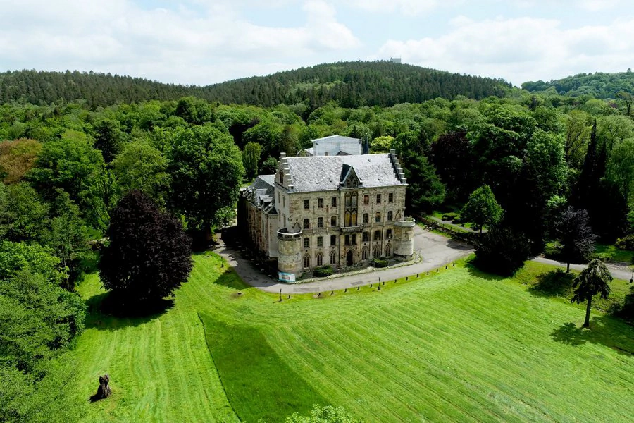 Luftaufnahme eines Schlosses, umgeben von üppigen Bäumen und einer großen Wiese.