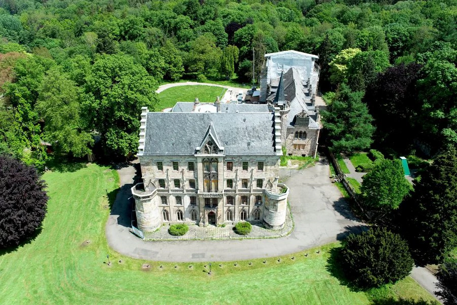 Luftaufnahme eines Schlosses, umgeben von üppigen Bäumen, die eine malerische Landschaft bilden.