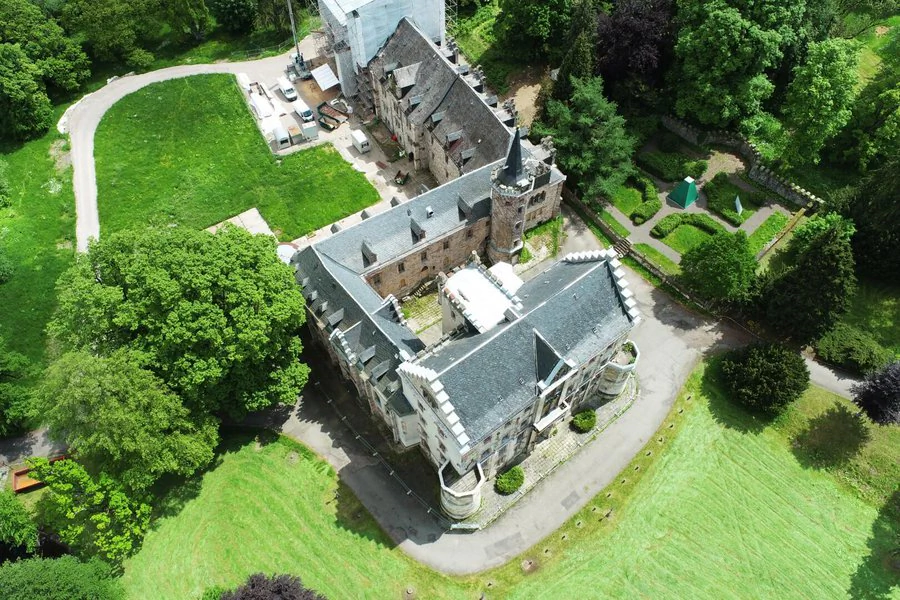 Luftaufnahme eines Schlosses mit einem Turm und einem Innenhof, umgeben von grüner Landschaft
