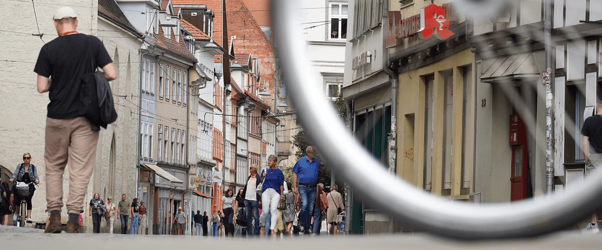 Bildbeschreibung / description: Ein Mann auf einem Fahrrad fährt durch eine schmale Straße, die von Häusern gesäumt und vielen Menschen gezeichnet ist