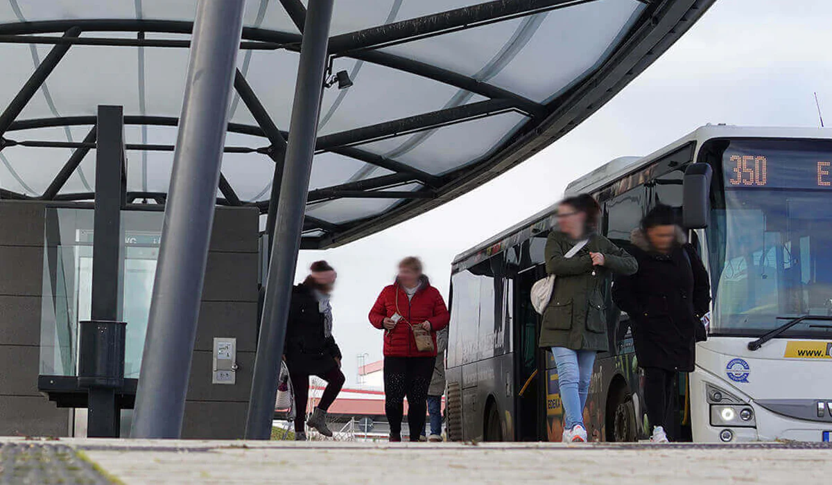 Bildbeschreibung / description: Menschen steigen an einer Bushaltestelle ein und aus einem Bus, während andere auf der Straße warten, Logo des Wirtschaftsministeriums Thüringen unten Links